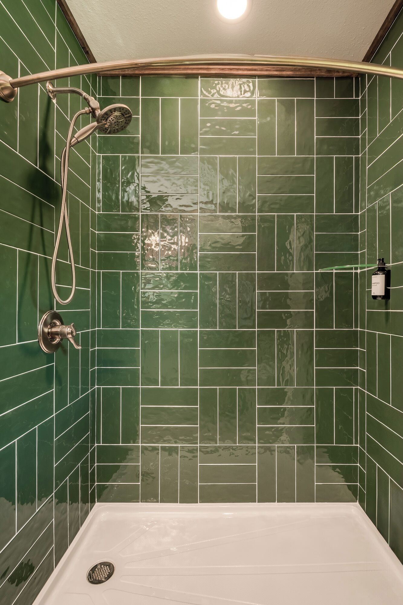 A bathroom with green tiled walls, a shower with a handheld showerhead, and a white bathtub.