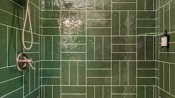 A bathroom with green tiled walls, a shower with a handheld showerhead, and a white bathtub.