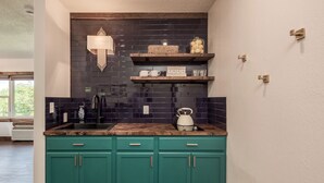 A kitchen with teal cabinets, a black backsplash, and a wooden countertop.