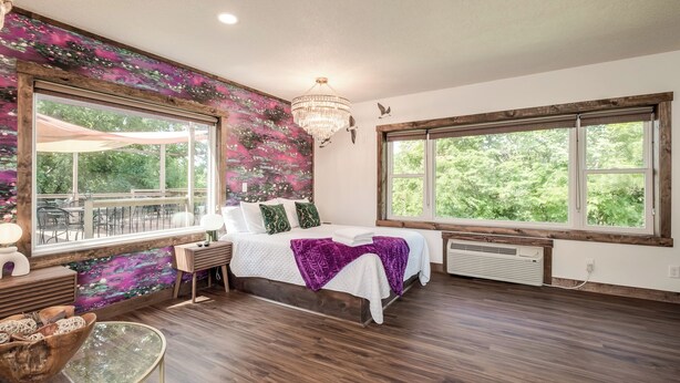 A bedroom with a large window, a chandelier, and a view of the outdoors.