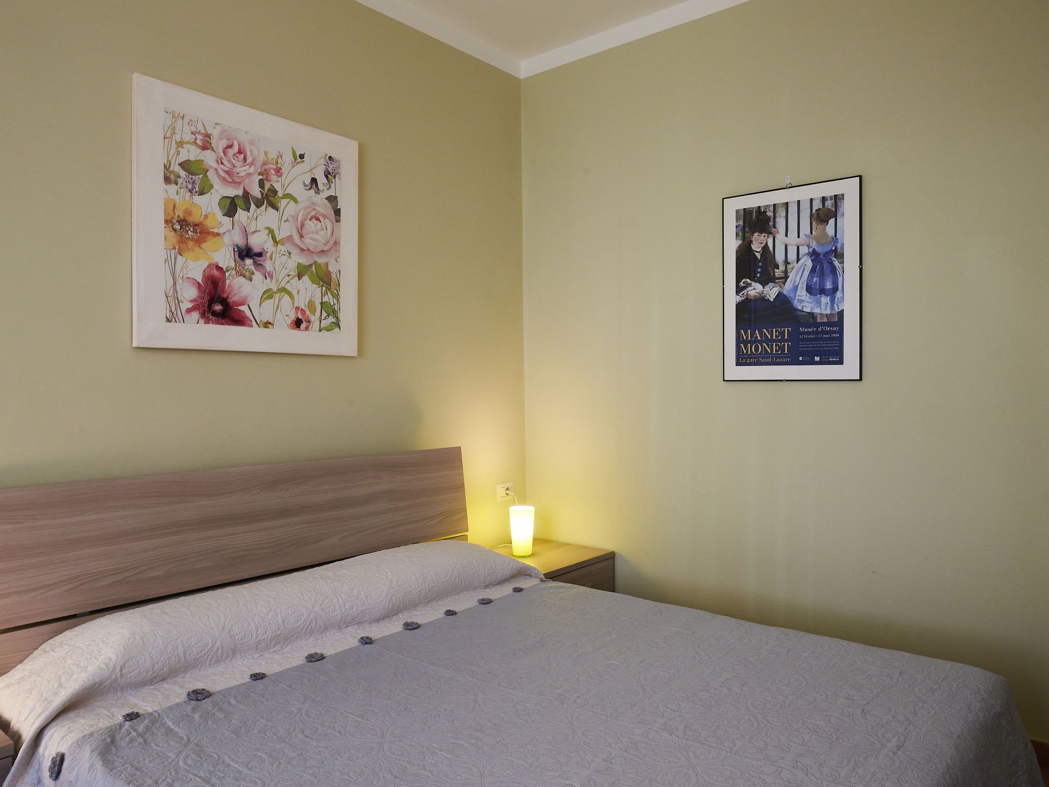 Quarto com cama, mesa de cabeceira, pôster e pintura na parede.