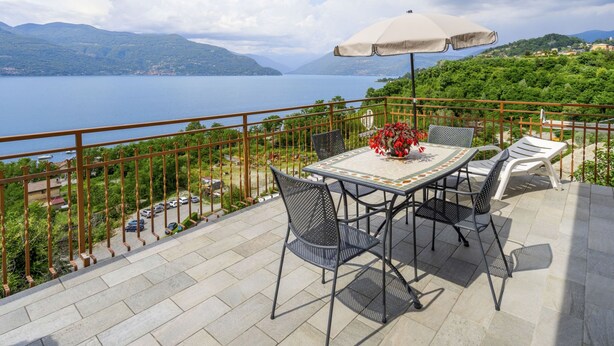 A terrace with a table and chairs, a potted plant, and a view of the sea and mountains. - Montesole by Interhome (Porto Valtravaglia)