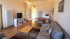 A living room with a sofa, coffee table, TV, and a dining area with a table and chairs. - Apartment Roma by Interhome (Porto Valtravaglia)