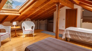 Ein gemütliches Schlafzimmer im Dachgeschoss mit Holzbalken, einem Oberlicht, einem Korbstuhl, einem kleinen Tisch und einem Bett.