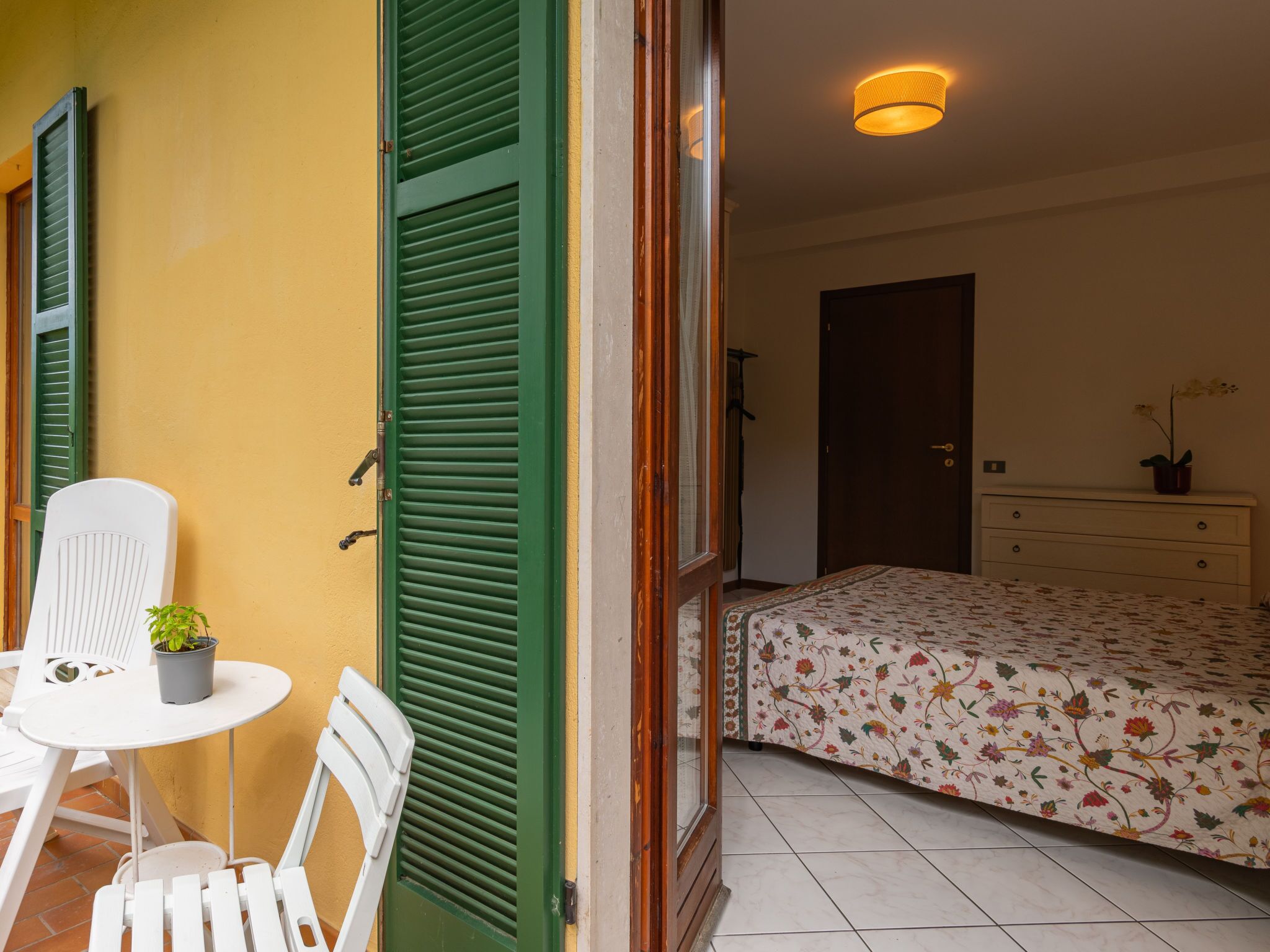 A room with a bed, a dresser, a chair, and a small table with a plant.