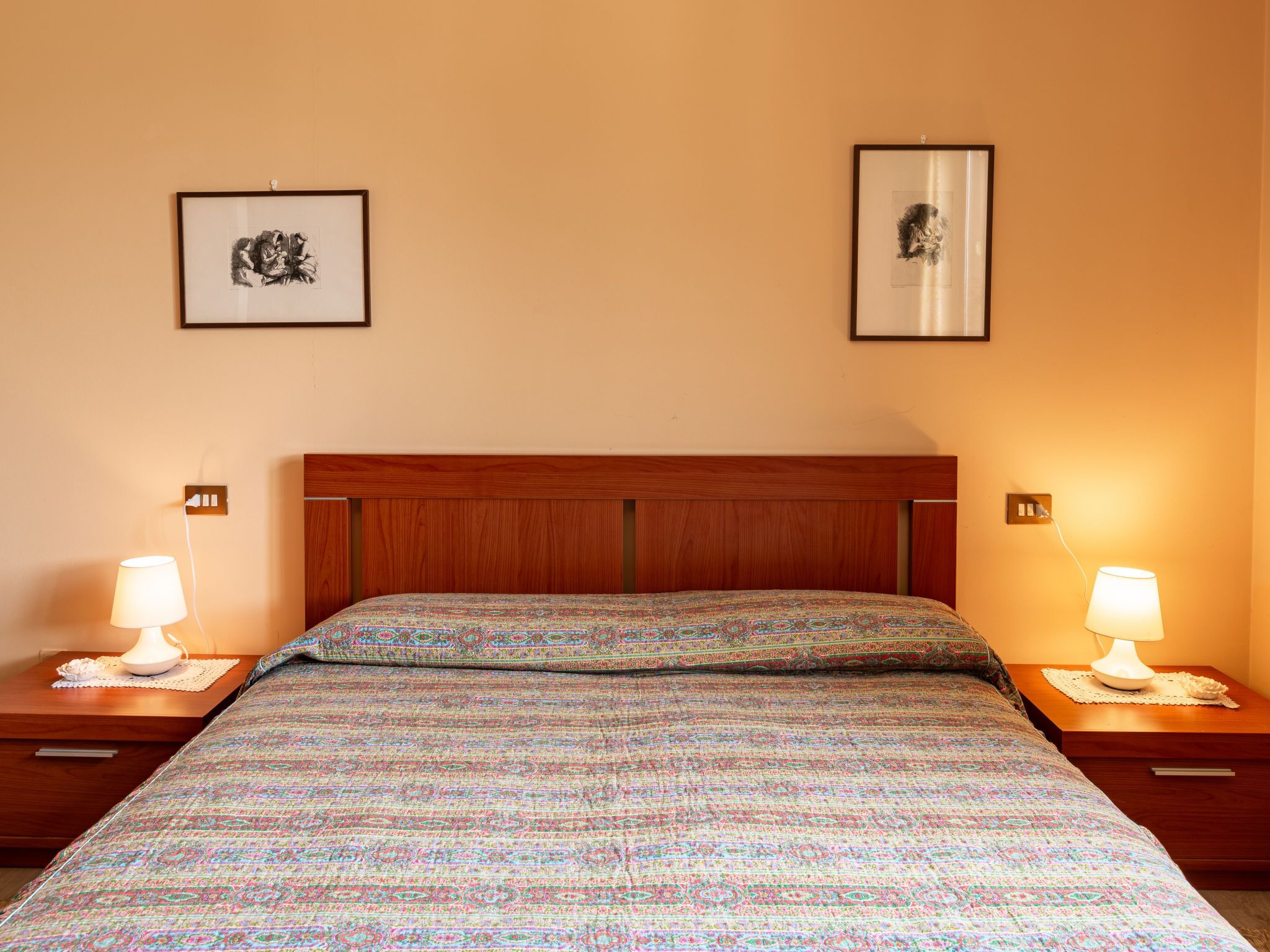 Una cama bien hecha con una colcha estampada, dos lámparas de noche y dos cuadros en la pared.