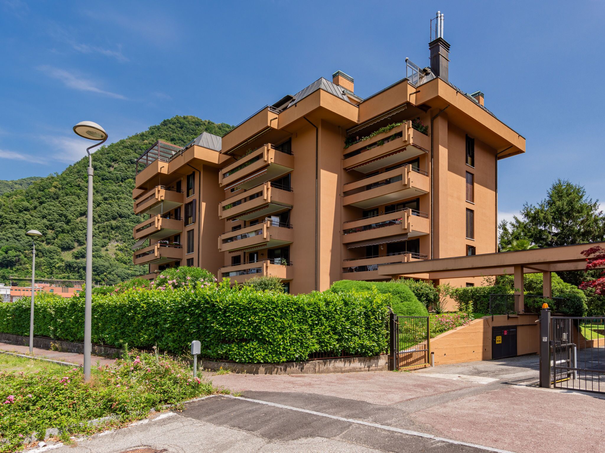 A multi-story residential building with balconies, a parking area, and a landscaped garden.