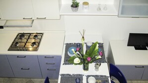A kitchen with a stove, a dining table set with blue plates and a vase with flowers. - Cielo e Mare (FLG111) by Interhome (Finale Ligure)
