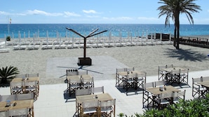 A beachside restaurant with outdoor seating, a palm tree, and a view of the ocean. - Cielo e Mare (FLG111) by Interhome (Finale Ligure)