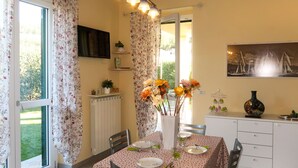 A dining area with a table set for two, a radiator, a TV mounted on the wall, and a window with curtains. - Apartment Roseto by Interhome (Cervo)