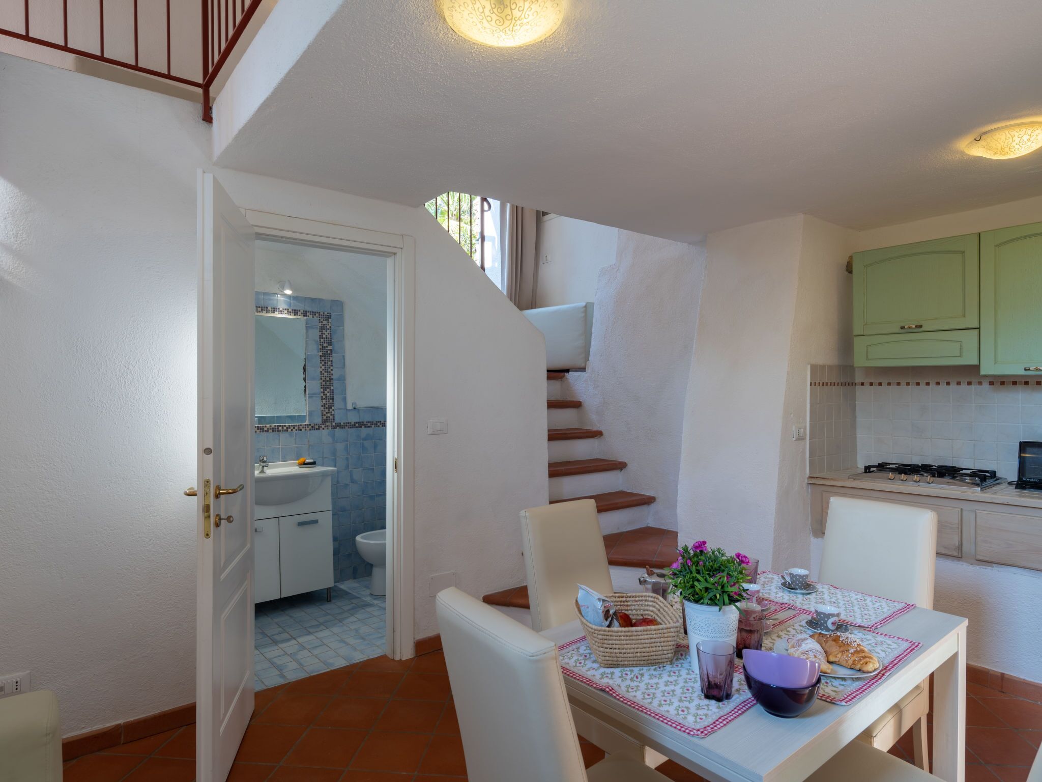Een kleine keuken met een eethoek, een trap en een badkamer, zichtbaar door een open deur.