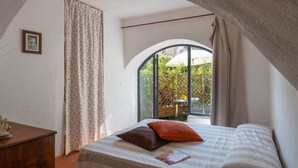 A bedroom with a bed, a wooden dresser, a framed picture, and a window with a view of greenery. - Annina (DOL285) by Interhome (Dolcedo)