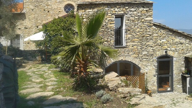 A stone building with a circular tower, a palm tree, and a stone pathway. - Annina (DOL285) by Interhome (Dolcedo)