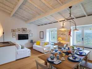Un coin repas avec une table en bois dressée pour quatre personnes, un canapé blanc et un téléviseur fixé au mur.
