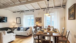 Un'ampia zona giorno con un tavolo da pranzo in legno apparecchiato per un pasto, un divano e un televisore fissato alla parete.