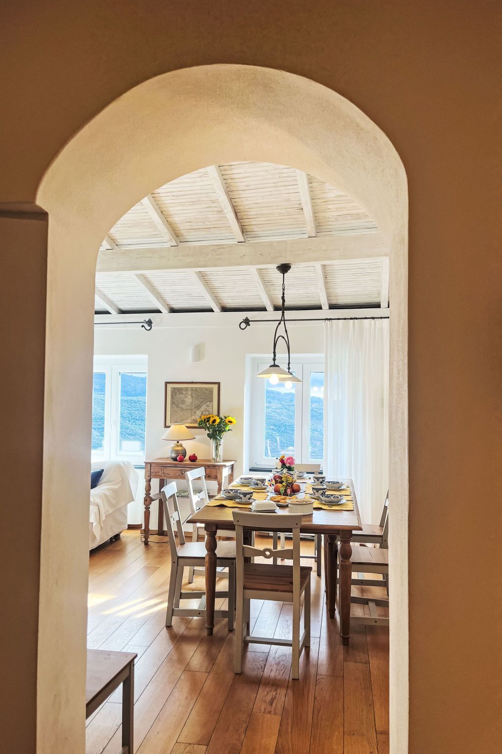 Un comedor con una mesa de madera dispuesta para cuatro personas, rodeada de sillas. Un arco de entrada da a otra habitación.