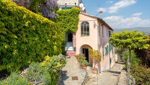 Un edificio tradizionale in pietra con facciata rosa, persiane verdi e un vialetto in pietra che conduce all'ingresso.