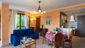 Un salon chaleureux avec un canapé bleu, une table à manger avec des chaises et, au fond, un coin cuisine.