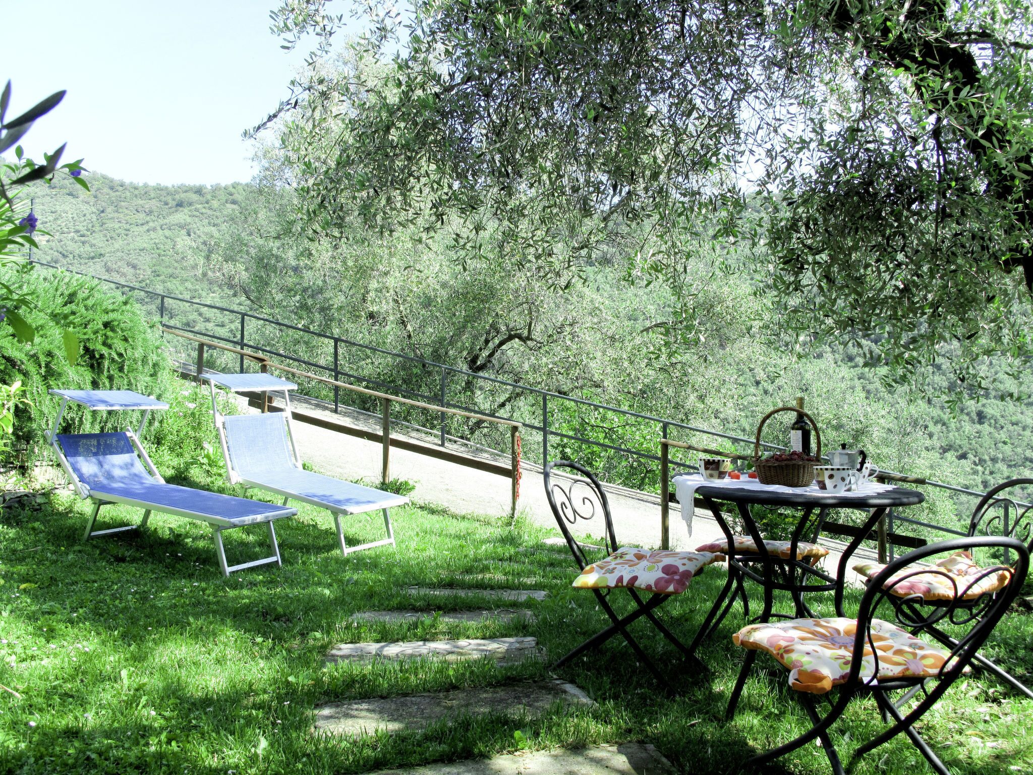 A patio with outdoor furniture, including a table and chairs, set against a backdrop of lush greenery and hills.