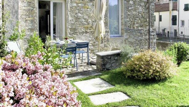 Un bâtiment en pierre doté d’une terrasse, de sièges en plein air et offrant une vue sur un clocher en arrière-plan.