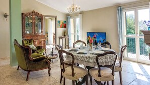 A dining room with a round table set for six, surrounded by six chairs. A large wooden cabinet with glass doors is against the wall, and a green armchair is visible in the foreground. - Settimo Cielo (DOL400) by Interhome (Dolcedo)