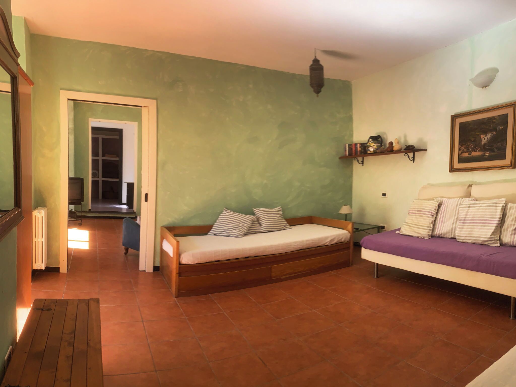 Ein Zimmer mit einem Bett, einem Schlafsofa, einer Heizung, einem Fernseher und einer Tür zu einem anderen Raum.