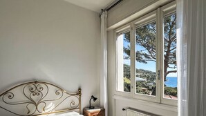 A bedroom with a metal bed frame, a view of the sea through a large window, and a radiator. - Alfreda (SLR101) by Interhome (San Lorenzo al Mare)