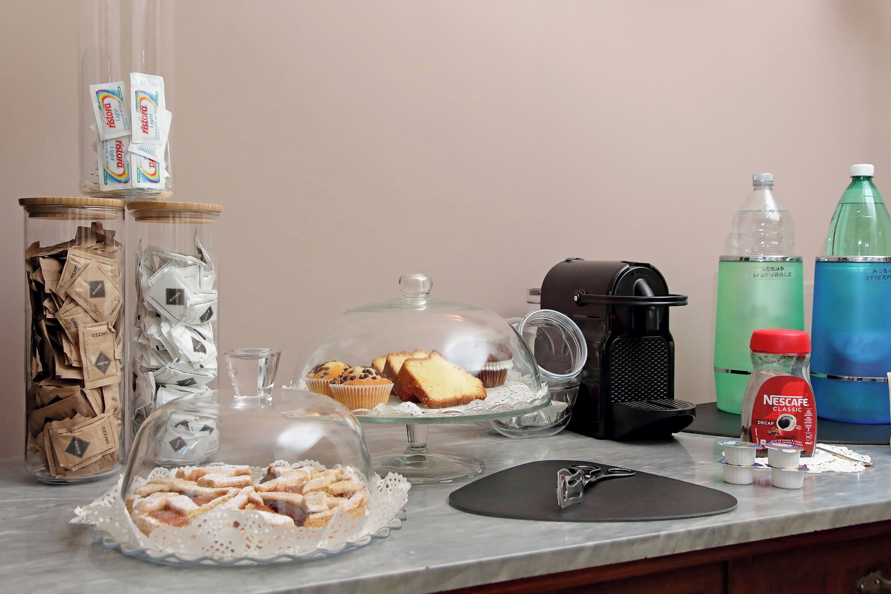 Uma bancada de cozinha com diversos itens, incluindo uma cafeteira, café Nescafe Classic, um bebedouro e alimentos em recipientes de vidro.