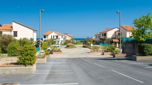 Un carrer residencial a la costa, amb cases, cel blau i un cotxe aparcat.
