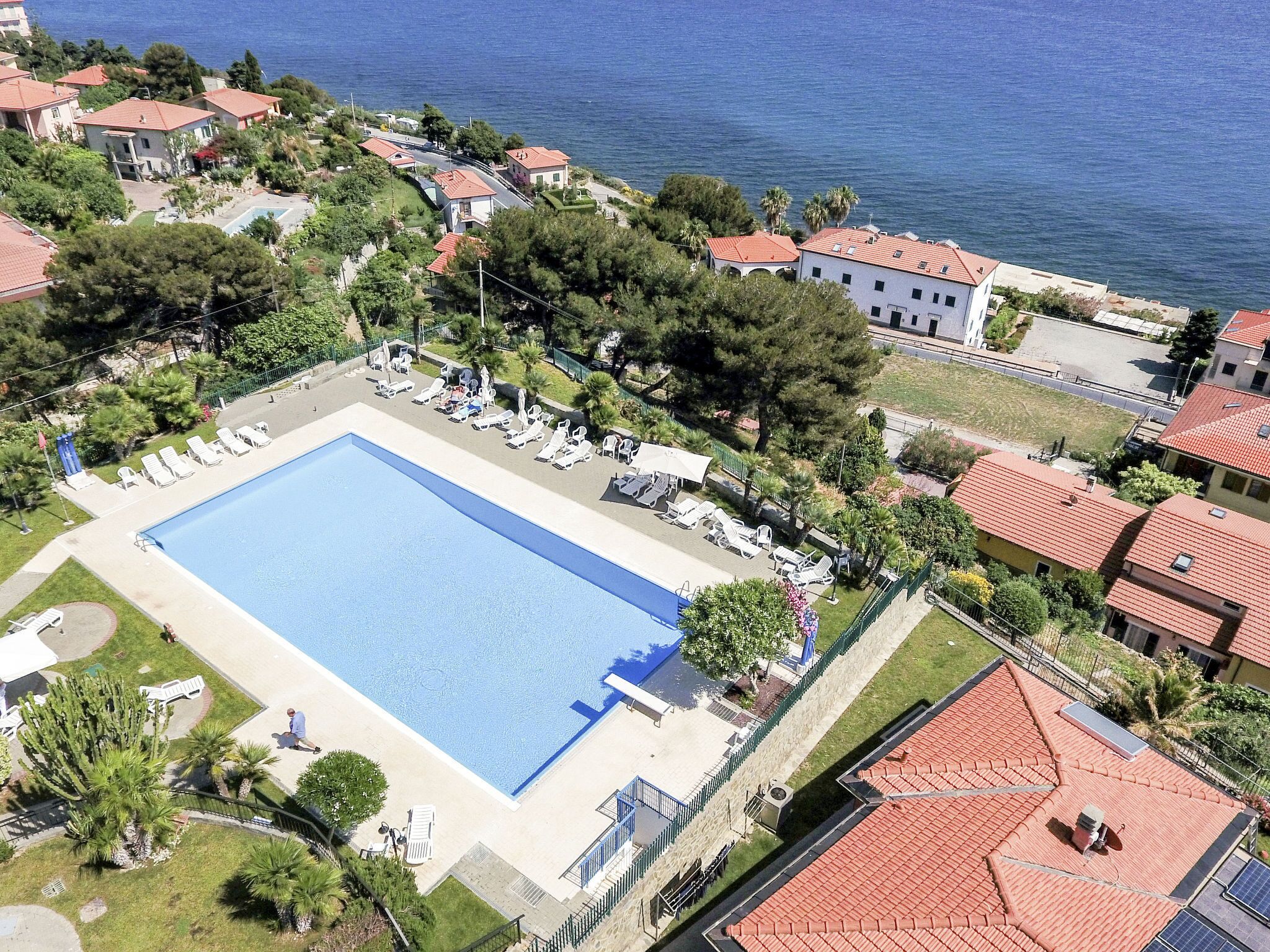 Vue aérienne d’un complexe hôtelier doté d’une grande piscine, entourée de chaises longues et de quelques arbres.
