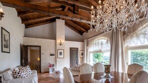A dining area with a wooden table and chairs, a chandelier, and a view of greenery outside. - Villa Carlotta by Interhome (Costigliole d'Asti)
