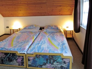 En dubbelsäng med ett sängöverkast med molnmönster i ett rum med synliga träbjälkar i taket, två sänglampor och ett fönster med gardiner.