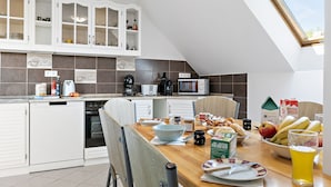 Une cuisine moderne avec des meubles blancs, une table à manger où sont disposés des aliments pour le petit-déjeuner, et une lucarne.