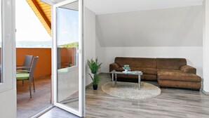 Un salon moderne avec une porte-fenêtre coulissante donnant sur un balcon, un canapé marron, une petite table avec une plante et un fauteuil vert.