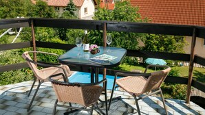 Un balcon avec des fauteuils en osier, une table et une bouteille de vin.