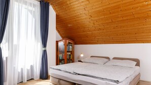 Une chambre avec un plafond en bois, un lit avec un matelas gris, une table de chevet avec une lampe et une bibliothèque.