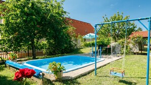 Une piscine à bordure bleue, entourée d’herbe et d’arbres.