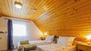 A cozy bedroom with a sloped ceiling, a bed with patterned bedding, two bedside tables with lamps, and a window with curtains. - Annemarie by Interhome (Balatonalmadi)