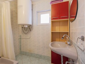 Un baño con lavamanos blanco, muebles rojos, cortina de ducha y ventana.