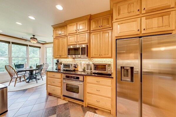 Una cocina con armarios de madera, electrodomésticos de acero inoxidable y una zona de comedor con sillas y una mesa.