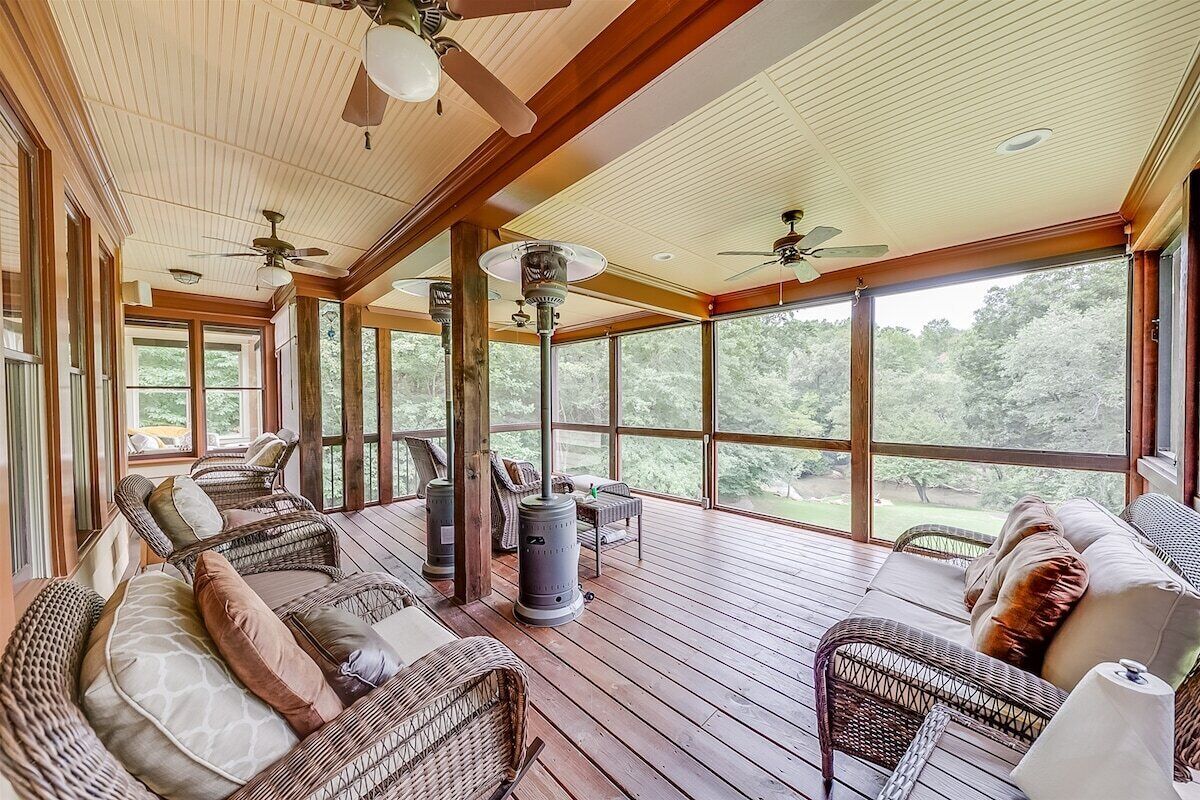 A covered porch with wicker furniture, ceiling fans, and large windows.