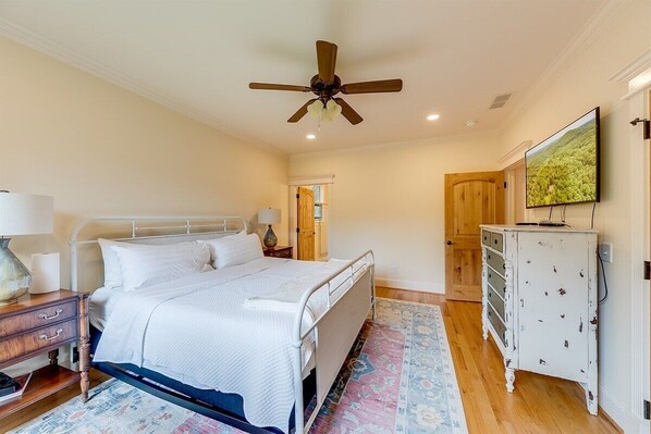 A bedroom with a bed, bedside tables, a ceiling fan, a dresser, and a television.