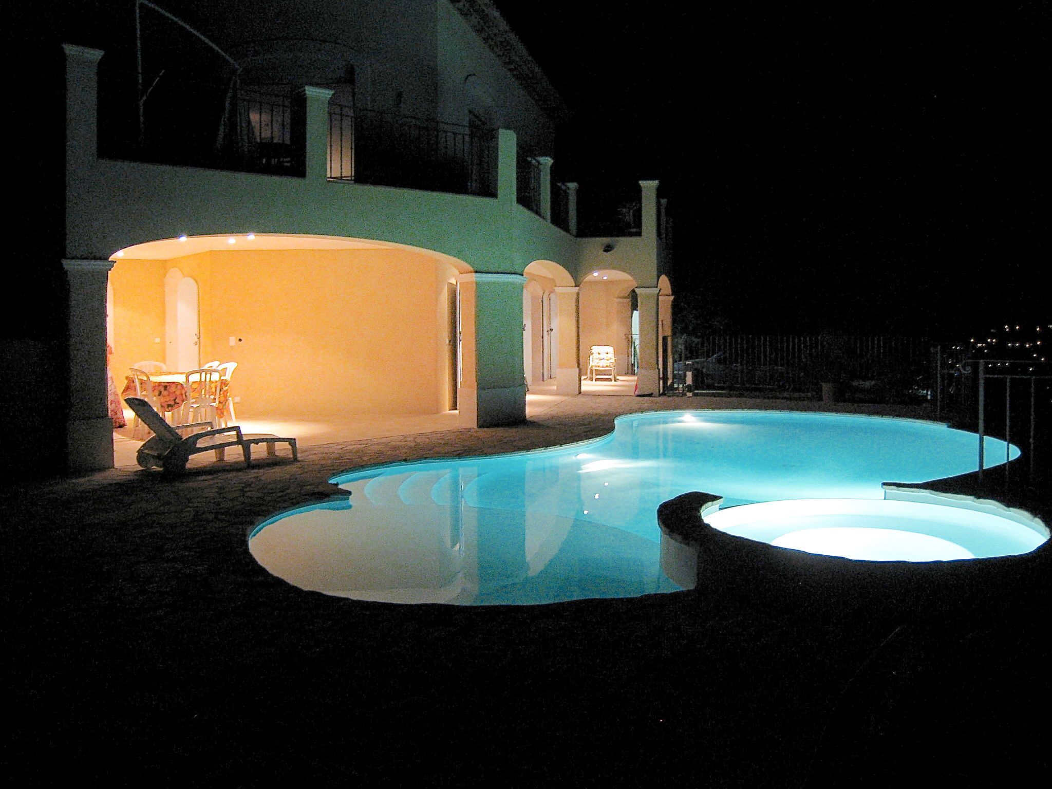 Una piscina de borde curvo, una silla de descanso y un edificio con zona de patio abierta.