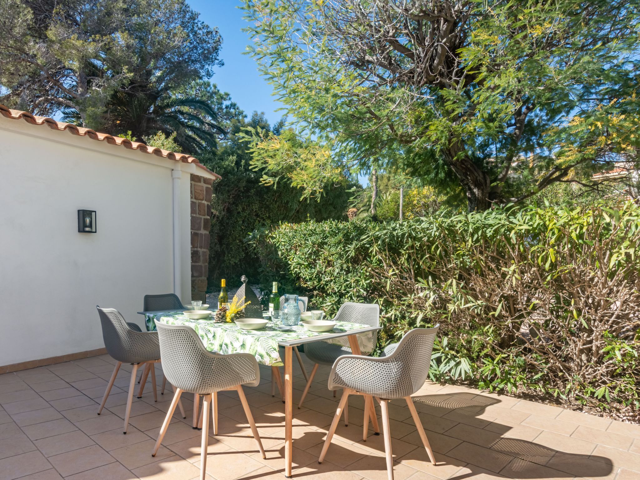 Een buitenpatio met een tafel voor vier personen, omringd door stoelen en een lage muur met een raam.