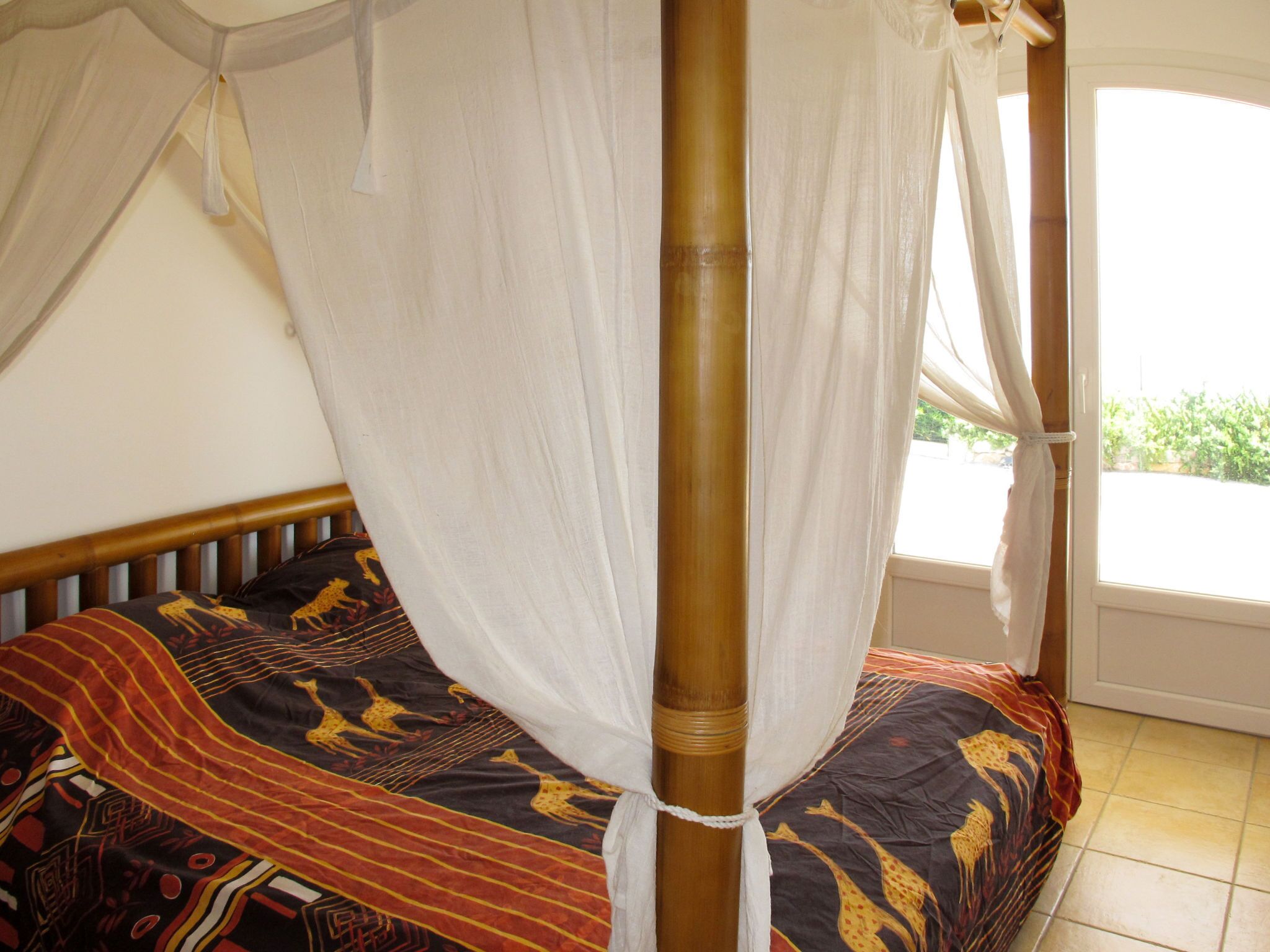 A bed with a canopy, a patterned bedspread, and a window with a view of greenery.