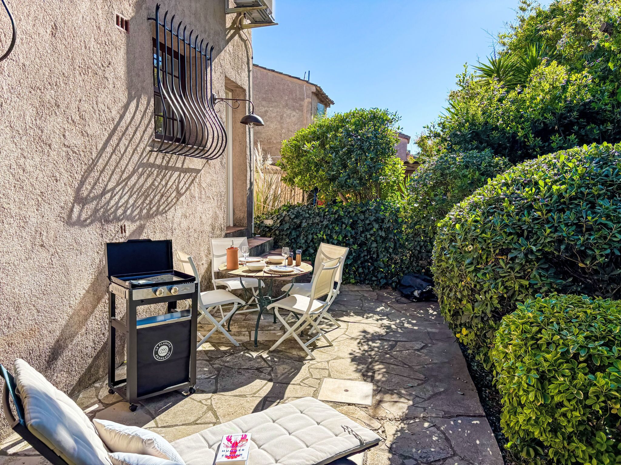 An outdoor patio with a grill, dining table, chairs, and a cushioned lounge area.