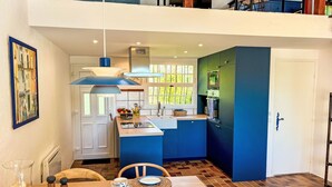 Een moderne keuken met blauwe kastjes, een eethoek met een houten tafel gedekt voor ontbijt, en uitzicht op de omgeving door een raam.