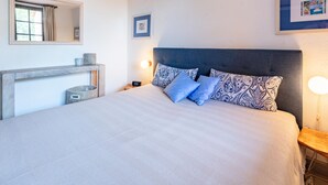 Een slaapkamer met een groot bed, een nachtkastje, een spiegel en een aan de muur bevestigd schilderij.