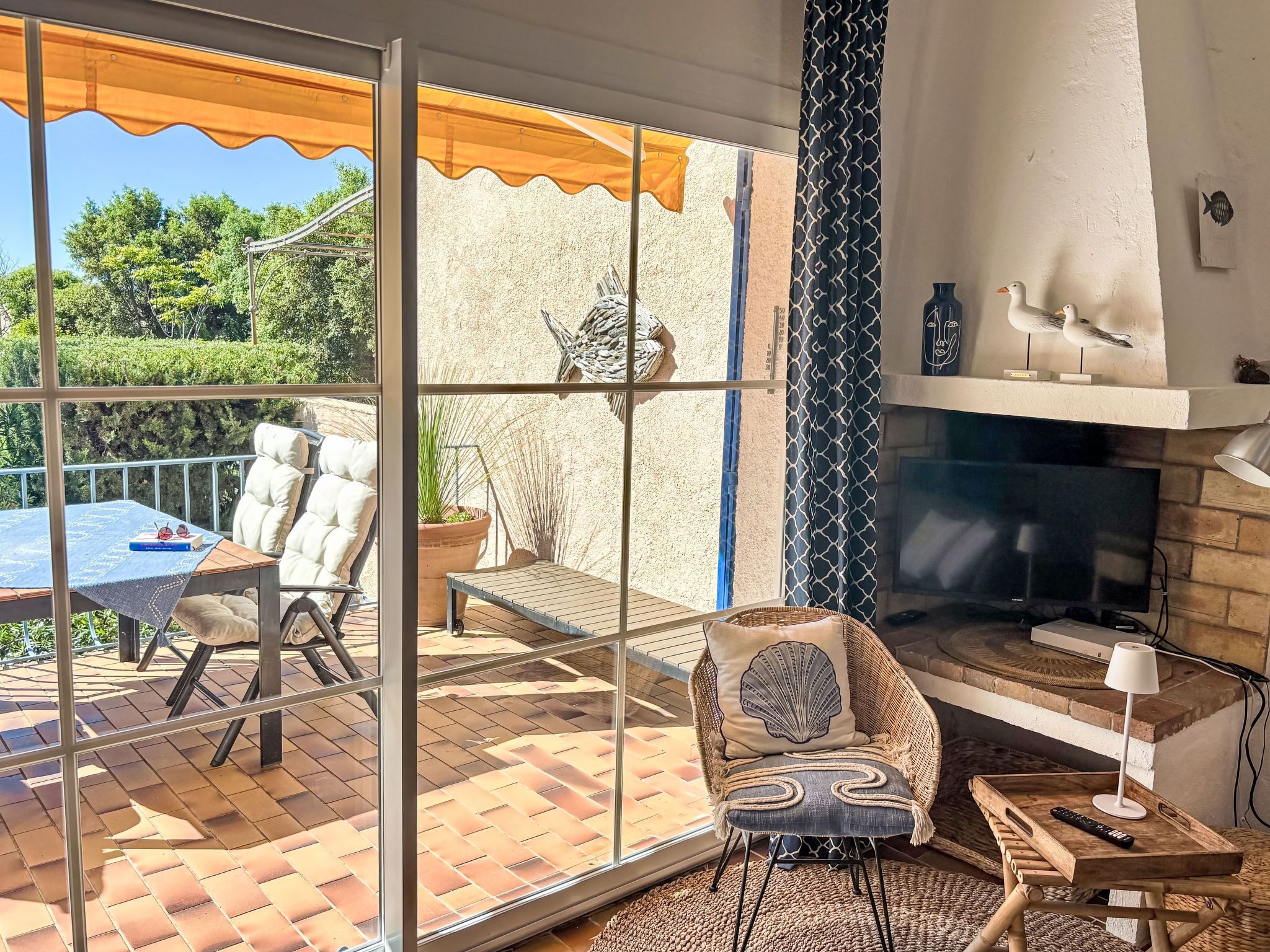 Habitación con puerta de vidrio que da a un patio exterior, chimenea, una silla de mimbre y una mesa con control remoto.