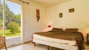 A bedroom with a large bed, a chair, and a view of greenery outside. - Villa Faro by Interhome (Montfort)